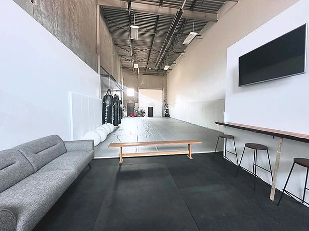 Members lounge seating beside the open mat training area at Mission BJJ